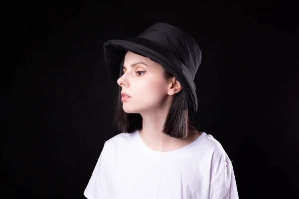 cute woman in white t-shirt and black panama hat, portrait on dark background
