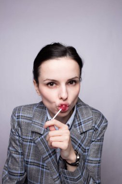 Lolipop yiyen iş kadını, gri arka plan