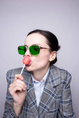 Kafesteki kadın yönetici ve yeşil gözlükler lolipop yiyor.