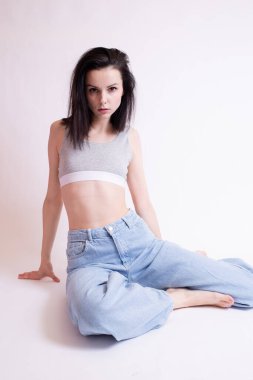 Mavi kotlu ve spor bluzlu kadın oturuyor, beyaz stüdyo geçmişi var.