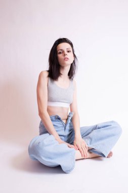 Mavi kotlu ve spor bluzlu kadın oturuyor, beyaz stüdyo geçmişi var.