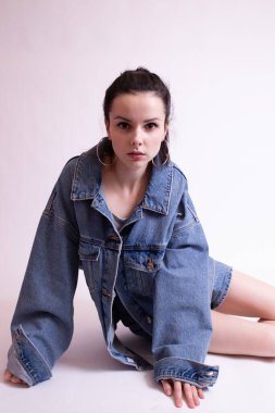 Beyaz stüdyo arka planında kot ceketli ve şortlu bir kadın.