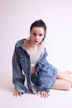 Beyaz stüdyo arka planında kot ceketli ve şortlu bir kadın.