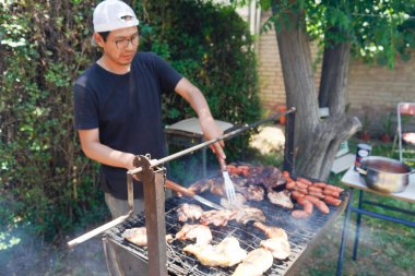 Genç adam tatilde ızgarada yemek pişiriyor.