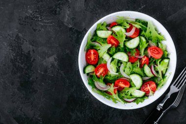 Sağlıklı yeşil salata, taze domates, salatalık, kırmızı soğan ve koyu taşlı arka planda marul. Üst görünüm, alanı kopyala.