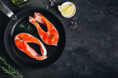 Dökme demir tavada taze çiğ somon bifteği pişirmeye hazır. Üst görünüm, karanlık taş arkaplanda boşluk kopyala.