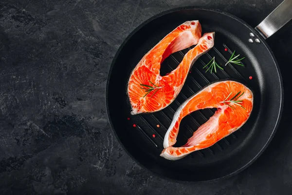 Dökme demir tavada taze çiğ somon bifteği pişirmeye hazır. Üst görünüm, karanlık taş arkaplanda boşluk kopyala.