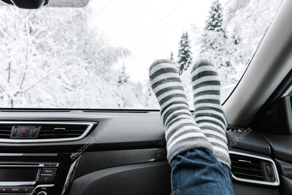 Woman feet in warm socks on car dashboard. Snow winter time, travel concept.