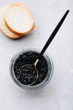 Cam kavanozda siyah havyar, beyaz taş arka planda kaşık, lüks lezzet aperatifleri.