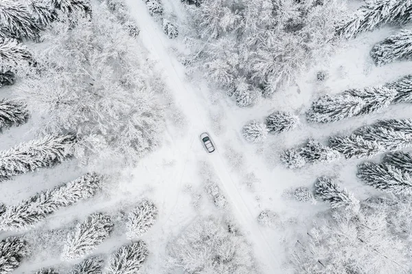 Aerial view of road with car in winter time, car driving in snow winter forest.