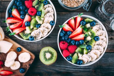 Sağlıklı taze meyve ve böğürtlen salatası, çilek, kivi, ahududu, muz ve chia tohumları ahşap arka planda beyaz kasede. Üst görünüm, alanı kopyala