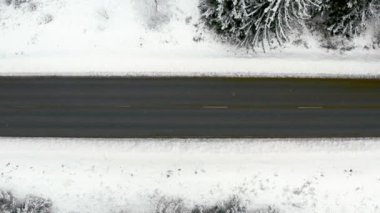 Kışın karla kaplı ormanda yol üzerindeki bir arabanın havadan görünüşü. Orman zemininde karla kaplı kış manzarası.