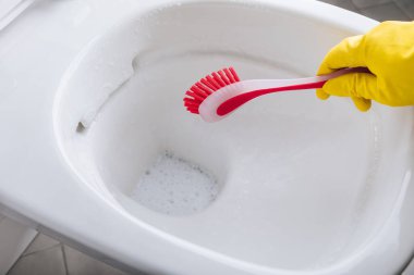 Sarı lastik eldivenli kadın kırmızı fırçalı klozeti temizliyor.