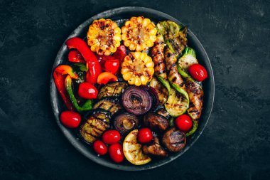 Koyu taşlı arka planda, tabakta ızgara sebzeler, üst manzara. Kabak, dolma biber, mısır, domates, kırmızı soğan ve patlıcan.