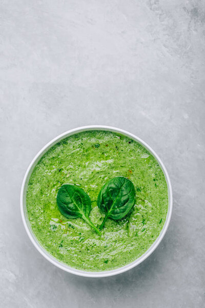Green creamy spinach soup on a gray concrete background. Healthy food and diet. Top view.