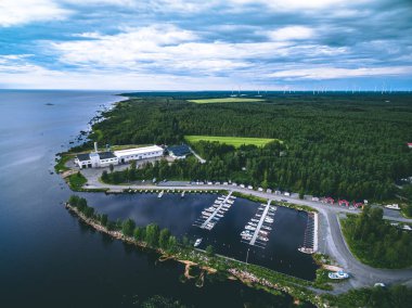 Mavi deniz ve yeşil ormanlı kuzey manzaralı hava manzarası. Ufukta balıkçı tekneleri ve yel değirmenleri olan küçük bir marina..