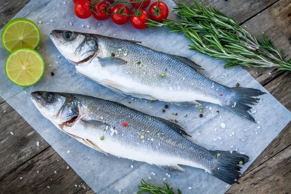 Zwei rohe Seebarsche mit Limette, Kirschtomaten und Rosmarin — Stockfoto