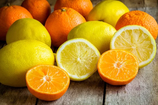 Ripe mandarins and lemons cut into a rustic wooden background — Stock Photo, Image