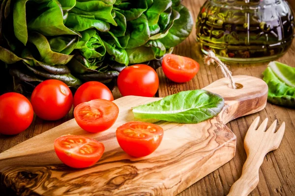 Tomates cereja na placa de corte de azeitona com alface orgânica verde — Fotografia de Stock
