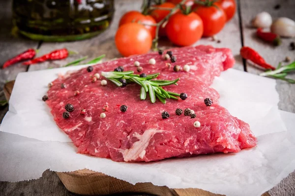 Raw meat steak on a cutting board with rosemary and cherry tomatoes — Stock Photo, Image
