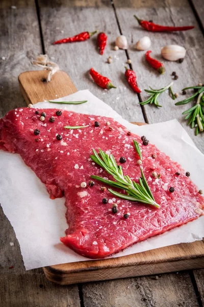 Steak de viande crue sur une planche à découper avec romarin, ail et poivre — Photo