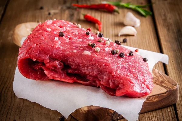 Raw meat steak on a cutting board with garlic and pepper — Stock Photo, Image