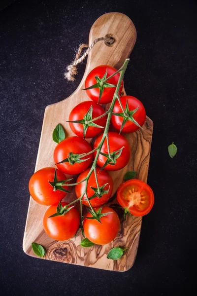 A bunch of fresh organic cherry tomatoes in olive cutting board — Stock Photo, Image