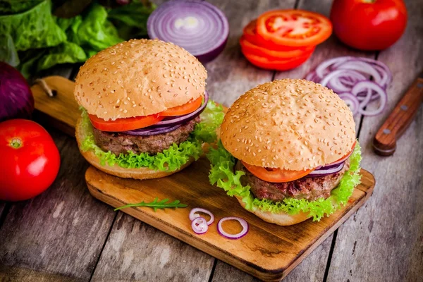 Twee zelfgemaakte hamburgers met verse biologische groenten op een rustieke achtergrond — Stockfoto