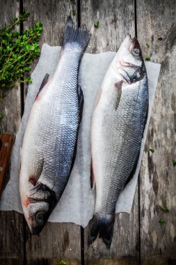 ahşap masa üzerinde taze kekik ile iki çiğ levrek