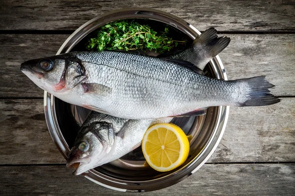 Two raw fresh sea bass in a bowl with thyme and lemon — Stock Photo, Image