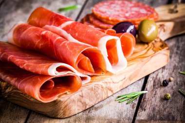 thin slices of prosciutto with olives and salami on a cutting board clipart