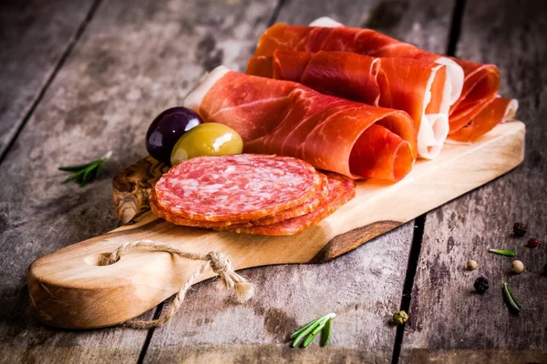 Thin slices of prosciutto with salami, olives and rosemary on a cutting board — Stock Photo, Image