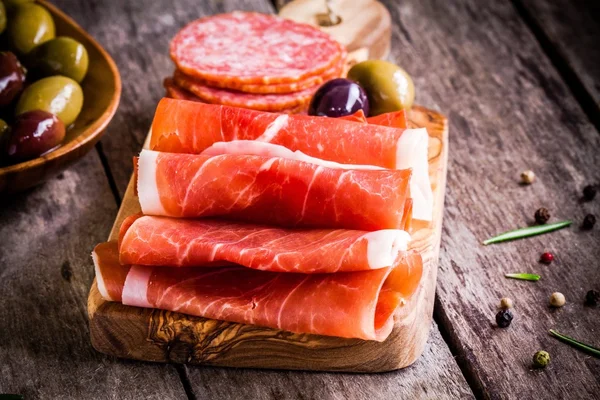 Rodajas delgadas de jamón con aceitunas y salami en una tabla de cortar —  Fotos de Stock