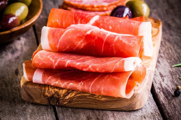 Thin slices of prosciutto with olives on a cutting board — Stock Photo, Image