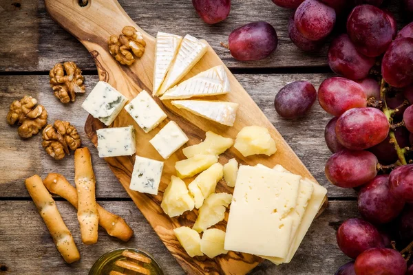 Prato de queijo: Emmental, queijo Camembert, queijo azul, paus de pão, nozes, uvas — Fotografia de Stock