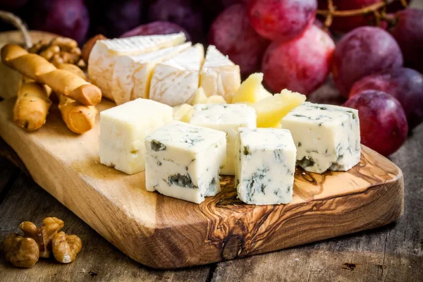 Placa de queso: Emmental, Camembert, Parmesano, primer plano de queso azul, con palitos de pan y uvas —  Fotos de Stock