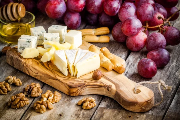 Piatto di formaggio: Camembert, parmigiano, formaggio blu, bastoncini di pane, noci, nocciole, miele, uva — Foto Stock