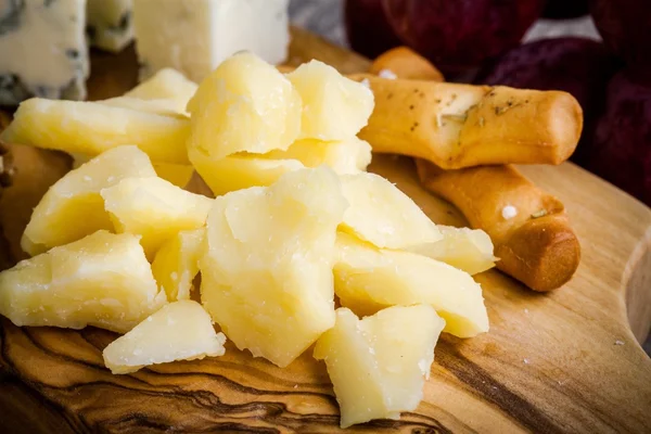 Сыр пармезан крупным планом с хлебными палочками на деревянной доске — стоковое фото