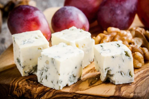 Синий сыр крупным планом с виноградом и орехами на деревянной доске — стоковое фото