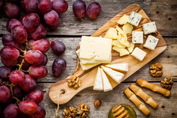 Placa de queso: Emmental, queso Camembert, queso azul, palitos de pan, nueces, avellanas, miel, uvas Imágenes de stock libres de derechos