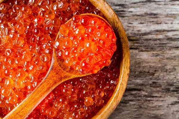 Caviar vermelho fresco em uma tigela de madeira com um closeup colher — Fotografia de Stock