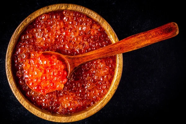 Fresh red caviar in a wooden bowl with a spoonful — Stock Photo, Image