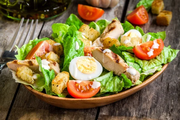 Insalata Cesare con crostini, uova di quaglia, pomodorini e pollo alla griglia in piatto di legno Foto Stock