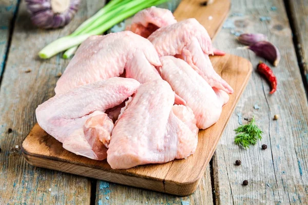 Alitas frescas de pollo crudo con ajo, cebolla y pimientos en una tabla de cortar — Foto de Stock