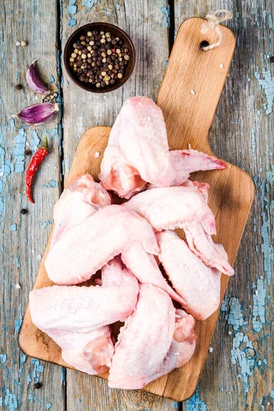 Asas de frango cruas frescas com alho e pimentas em uma tábua de corte — Fotografia de Stock