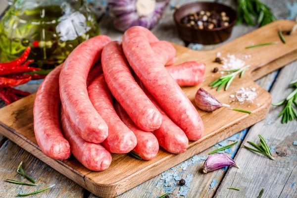 Rohe hausgemachte Würstchen auf Schneidebrett mit Rosmarin und Knoblauch — Stockfoto