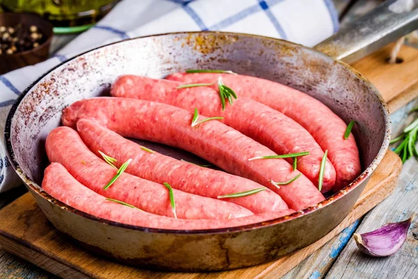 Embutidos caseros crudos en una sartén con romero — Foto de Stock