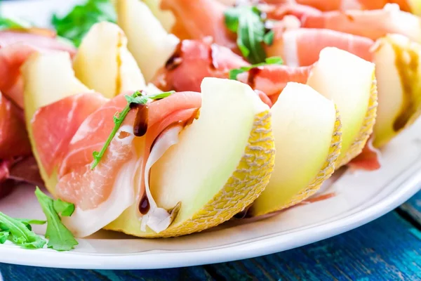 Salade de melon avec fines tranches de prosciutto, feuilles de roquette et sauce balsamique gros plan — Photo