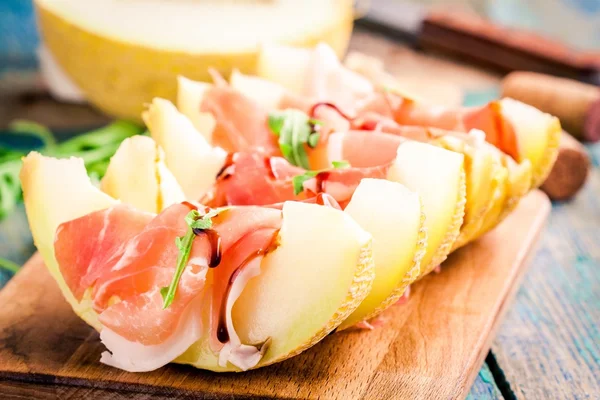 Melon with thin slices of prosciutto and arugula leaves — Stock Photo, Image