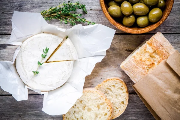 Whole Camembert cheese with thyme, olives and baguette — Stock Photo, Image